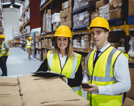 Two employees wearing safety gear smile in the warehouse