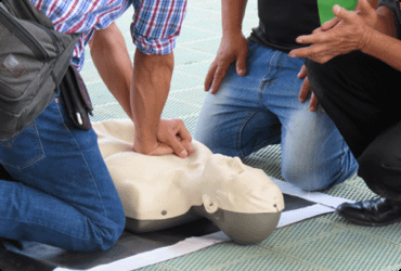 Two employees are instructed on how to properly perform CPR on a dummy