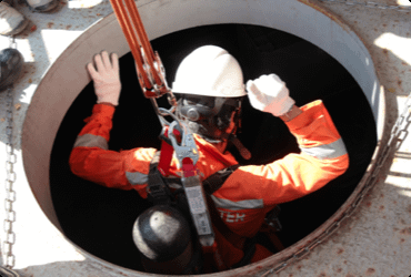 An employee is lowered into a confined space after completing their confined space entry course
