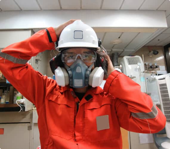 An environmental inspector with goggles and a helmet puts on a respirator